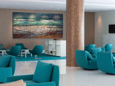 Area lounge moderna dell'hotel con poltrone blu, pavimento bianco e quadro del mare sulla parete