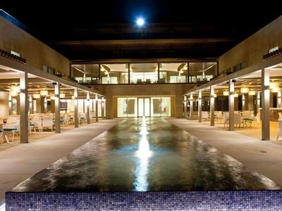 Cortile d'hotel con piscina illuminata e aree coperte per sedersi di notte