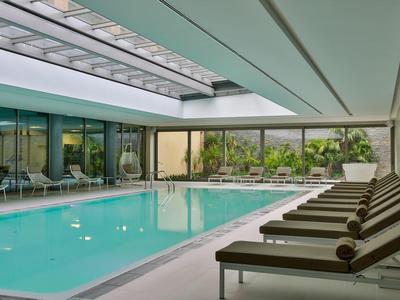 Piscina interna con lettini, soffitto moderno e grandi finestre con vista sul verde.
