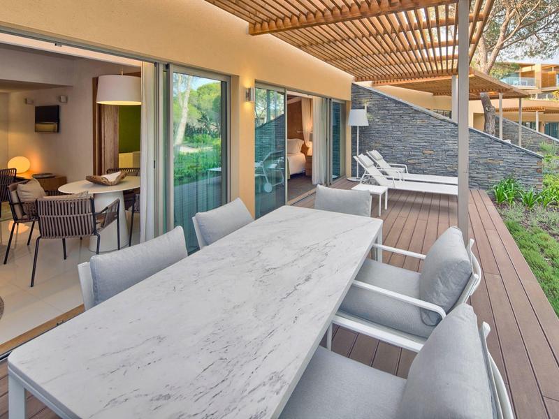 Terrazza con grande tavolo in marmo e sedie imbottite davanti a una camera d'hotel con vista mare.