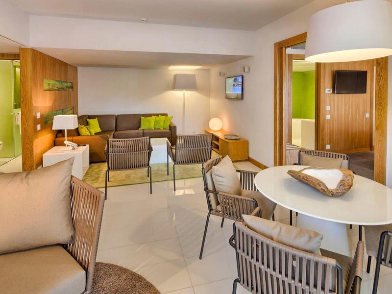 Camera d'hotel moderna con letto grande, coperta verde e vista su terrazza e natura