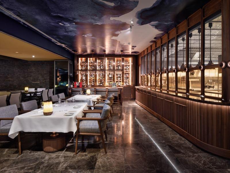 Ristorante elegante con tovaglie bianche, illuminazione soffusa e dettagli in legno.