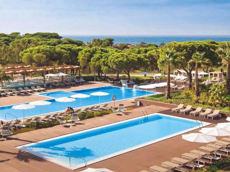 Piscina dell'hotel con lettini e vista sul mare circondata da alberi verdi.