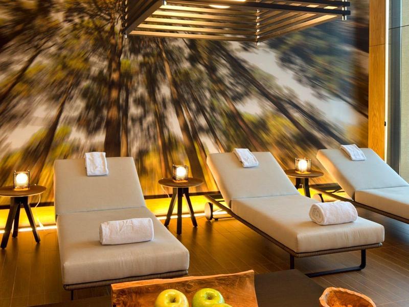 Sala relax con lettini, candele e una lampada moderna davanti a una parete con motivo albero.