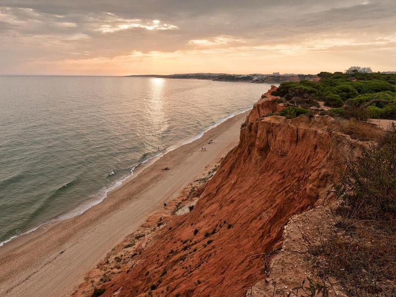 Scogliere rosse che si affacciano su una spiaggia tranquilla al tramonto.