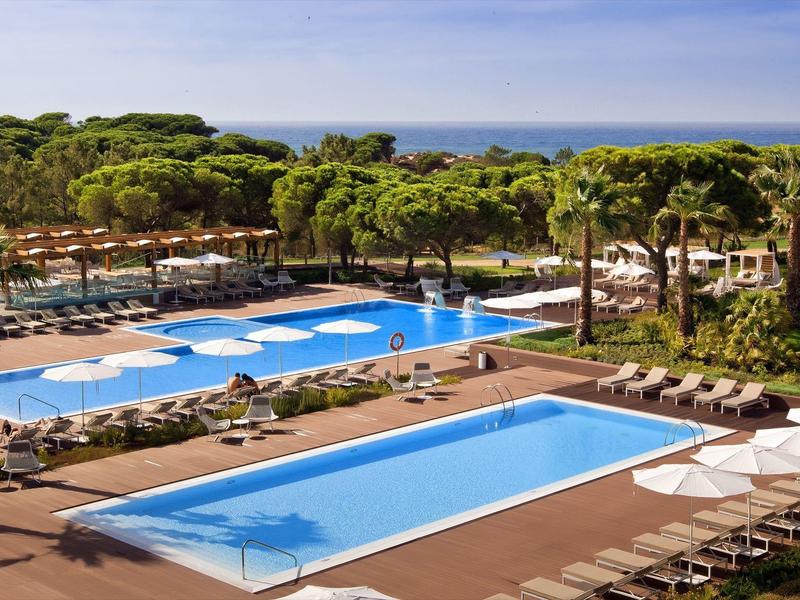 Due piscine con lettini e palme in un resort vicino al mare.
