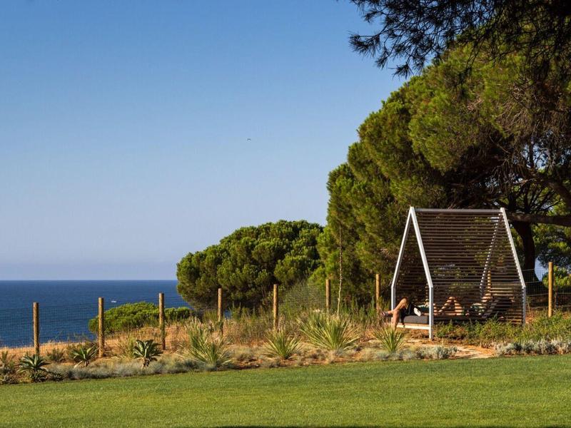 Giardino verde con altalena sotto gli alberi e vista mare con cielo limpido.