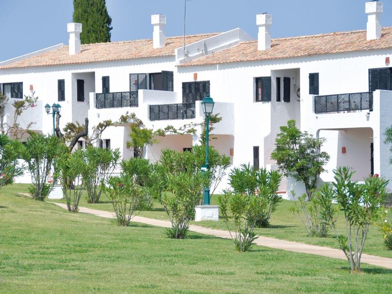 Weiße Reihenhäuser mit schwarzen Balkonen umgeben von grünem Rasen und Sträuchern bei blauem Himmel.