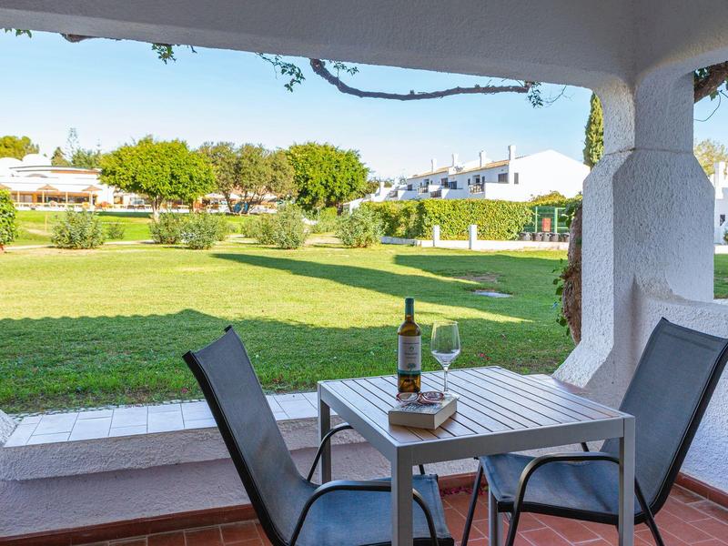 Terrasse mit Tisch, zwei Stühlen, Weinflasche, Gläsern und weiter grüne Rasenfläche mit Häusern.