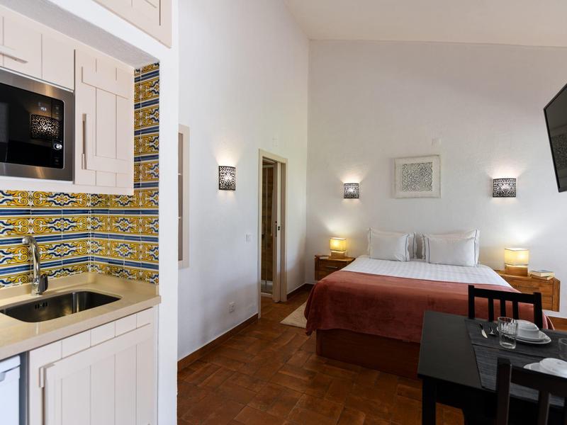 Helles Hotelzimmer mit Doppelbett, bunter Küchenzeile, Fernseher und kleinem Esstisch.