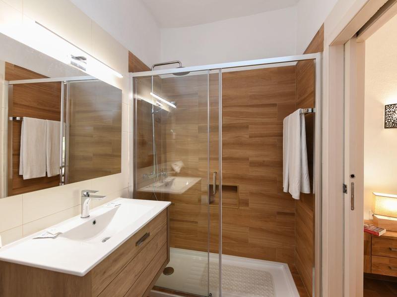 Helles Badezimmer mit Holzoptik-Dusche, Waschbeckenunterschrank, großem Spiegel und Handtüchern.