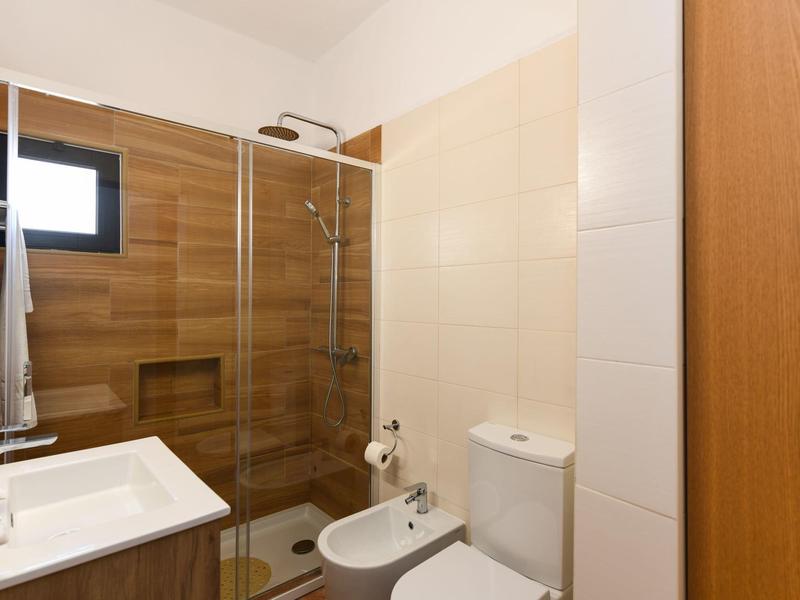 Kleine Badezimmer mit Dusche, Toilette, Bidet, Waschbecken und Holz- sowie hellen Wandfliesen.