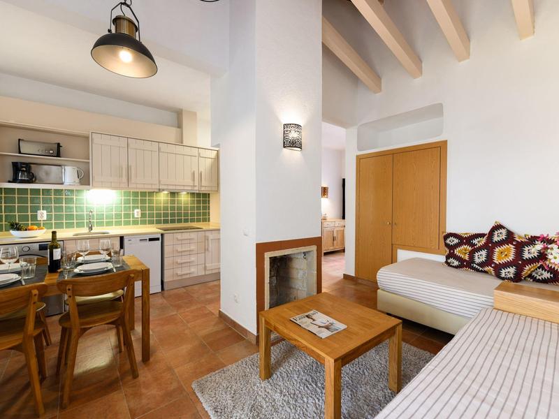 Gemütliches Wohnzimmer mit Holzmöbeln, weißem Sofa, Kamin und angrenzender Küche mit grün gekachelter Wand.