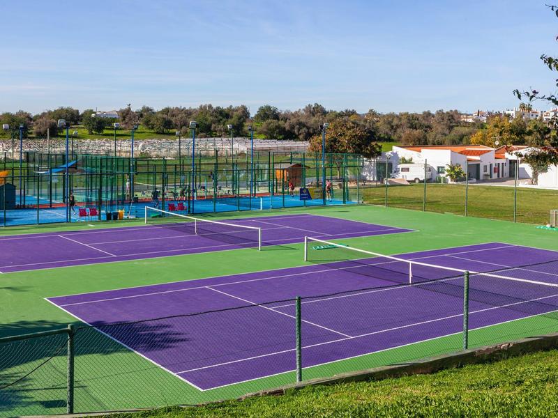 Mehrere Tennisplätze mit lila Spielflächen und grünem Rand unter blauem Himmel, umgeben von Grün.