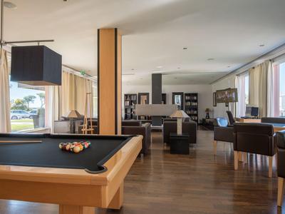 Moderne Lounge mit Billardtisch, Sesseln und großen Fenstern mit Blick ins Grüne.