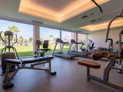 Fitnessraum mit Trainingsgeräten und großem Fenster mit Blick auf eine Grünfläche.