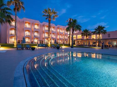 Beleuchtetes Hotel mit Pool und Palmen bei Abenddämmerung