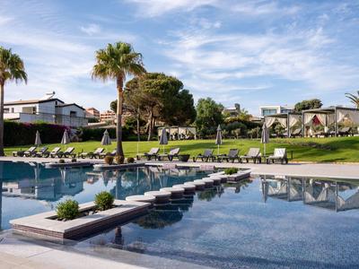 Moderner Hotelpool mit Palmen und Liegestühlen unter blauem Himmel.