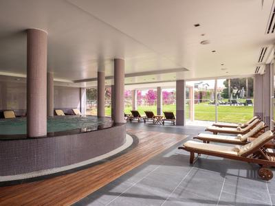 Moderner Wellnessbereich mit Rundbecken, Liegestühlen und Blick auf Gartenfläche