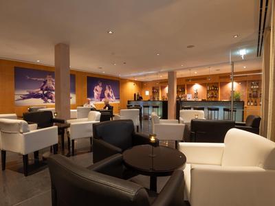 Eleganter Hotel-Loungebereich mit weißen und schwarzen Sesseln, Tischen und moderner Beleuchtung.