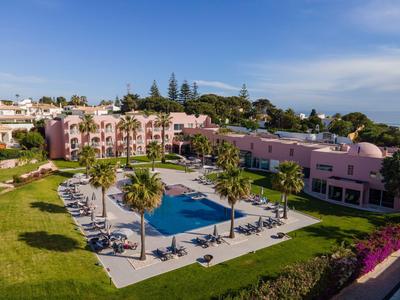 Hotelanlage mit rosa Gebäuden, Swimmingpool, Palmen und Liegestühlen unter blauem Himmel