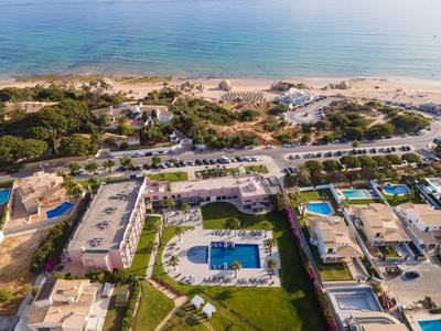 Luftaufnahme eines Strandresorts mit Pool, mehreren Gebäuden und Sandstrand am Meer