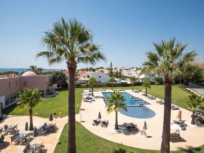 Hotelpool mit Liegestühlen, Palmen und Blick auf das Meer bei klarem Himmel
