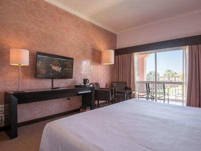 Hotelzimmer mit großem Bett, Schreibtisch, Fernseher und Balkon mit Gartenblick