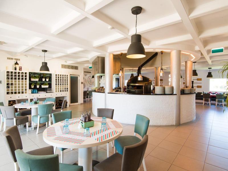 Helles Restaurant mit weißen Tischen, gepolsterten Stühlen und einer Kaffeebar in modernem Design.