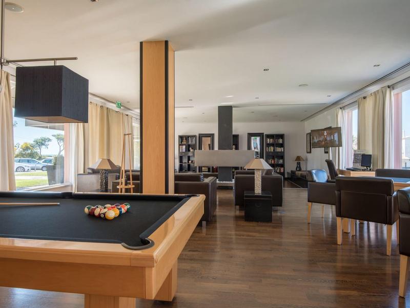 Moderne Lounge mit Billardtisch, Sesseln und großen Fenstern mit Blick ins Grüne.