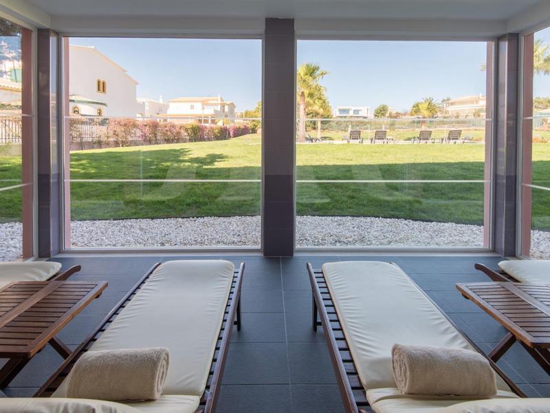 Zwei Liegen mit Handtüchern auf einer Veranda mit Blick auf gepflegten Rasen und Gebäude.