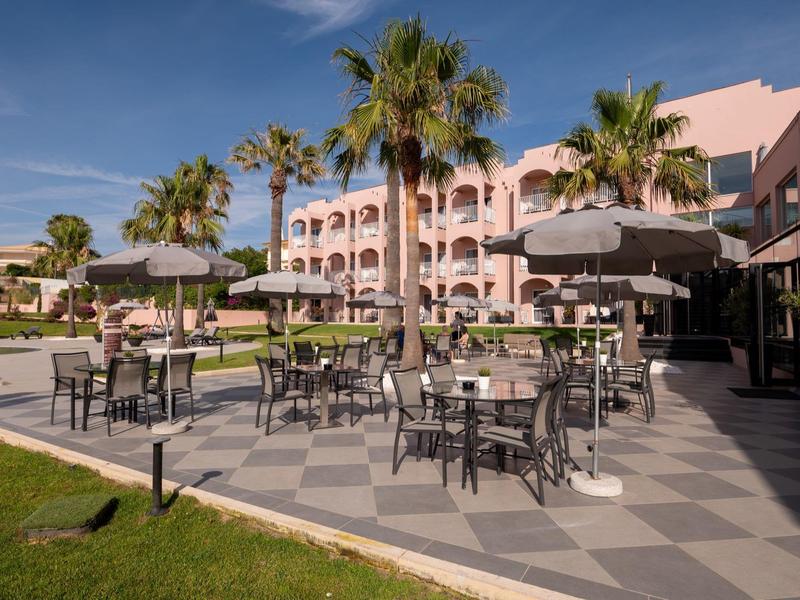 Hotelterrasse mit Tischen, Stühlen und Palmen bei klarem Himmel