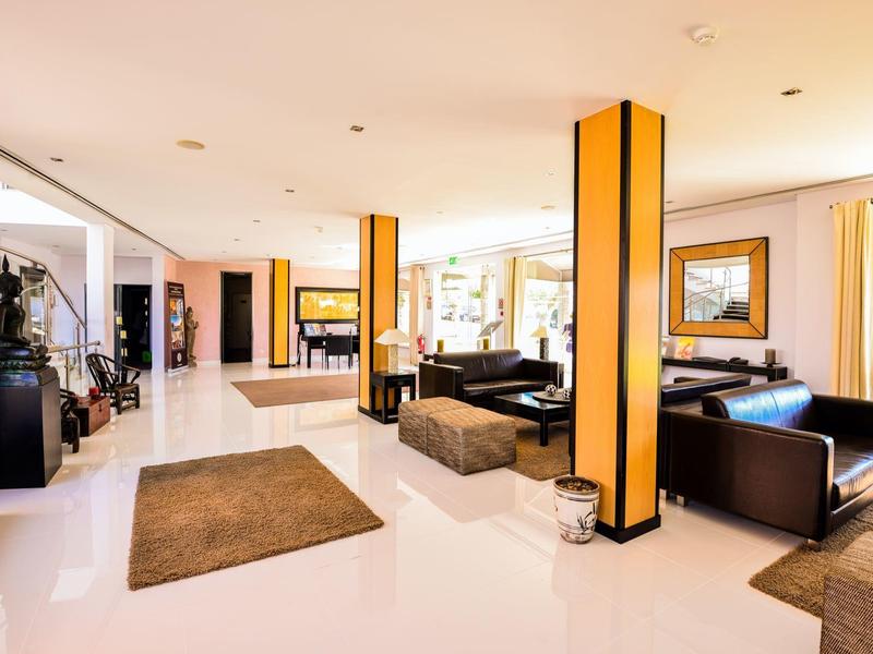 Helle Hotellobby mit gelben Säulen, schwarzen Sesseln und braunen Teppichen.