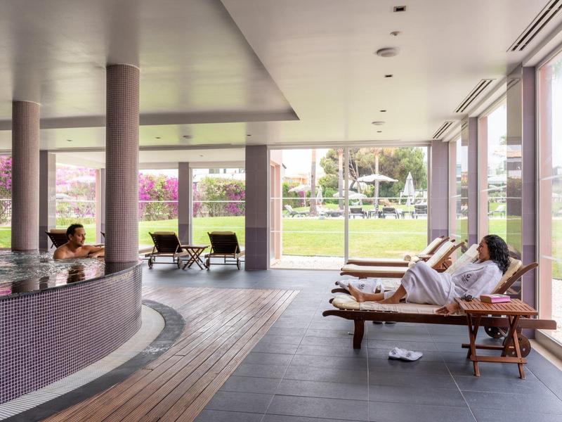 Ruhebereich mit Liegen und großen Fenstern, Blick auf eine grüne Außenanlage