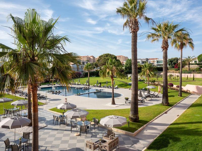 Moderner Poolbereich mit Liegestühlen und Palmen in einer Hotelanlage bei sonnigem Wetter