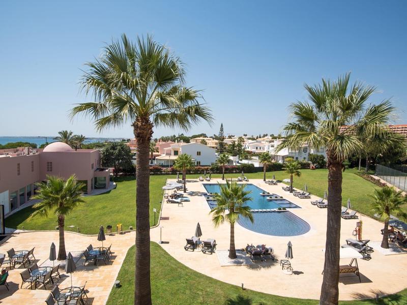 Hotelpool mit Liegestühlen, Palmen und Blick auf das Meer bei klarem Himmel
