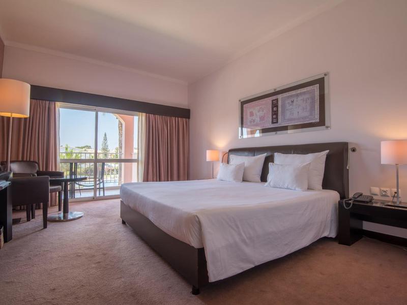 Modernes Hotelzimmer mit großem Bett, Schreibtisch, Balkon und mildem Licht