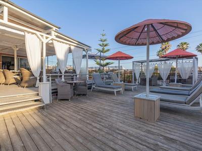 Große Holzterrasse mit Lounge-Möbeln und Sonnenschirmen in einem Hotel mit Meerblick.