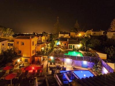 Nachtaufnahme eines beleuchteten Wohnkomplexes mit mehreren Pools und Gartenanlagen.