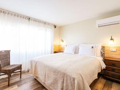 Helles Schlafzimmer mit Doppelbett, Holzstuhl, Nachttischen und Klimaanlage an heller Wand.