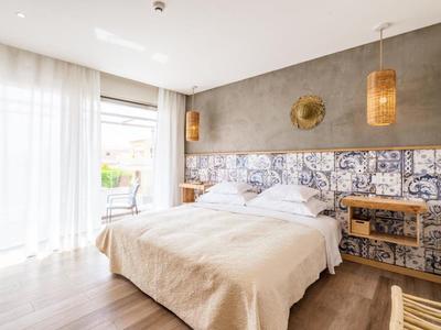 Helles Schlafzimmer mit großem Bett, gemusterter Wand, Holzlampe und Tageslicht durch breite Fenster.