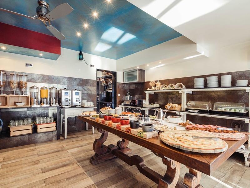 Ein heller Frühstücksraum mit gedecktem Holztisch und Buffetstationen an den Wänden.