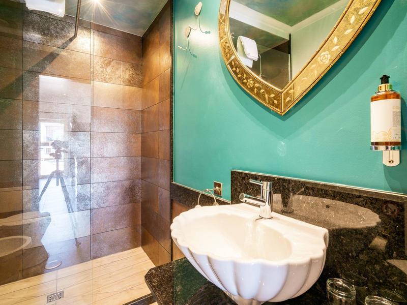 Badezimmer mit muschelförmigem Waschbecken, grünem Wandspiegel und einer Dusche mit Glaswand.