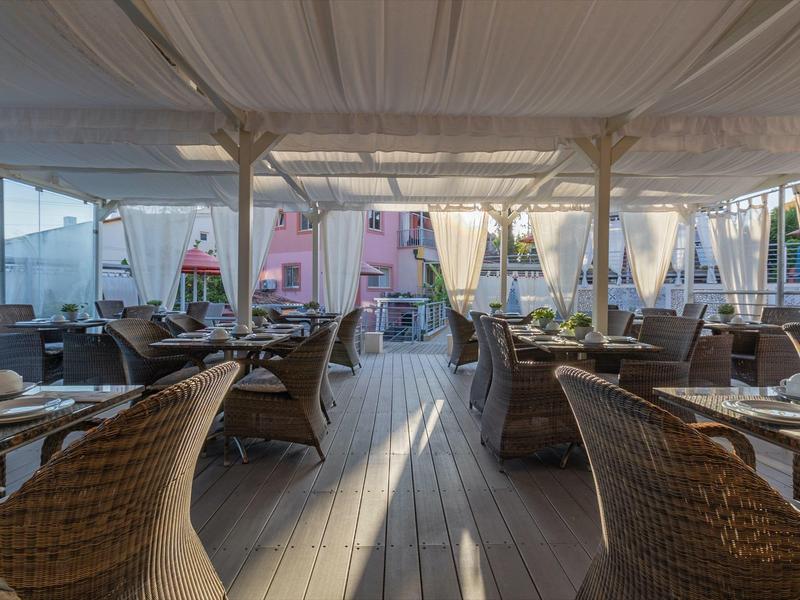 Überdachte Terrasse mit Sitzgruppen aus Korbmöbeln und gedeckten Tischen in einem Hotel.