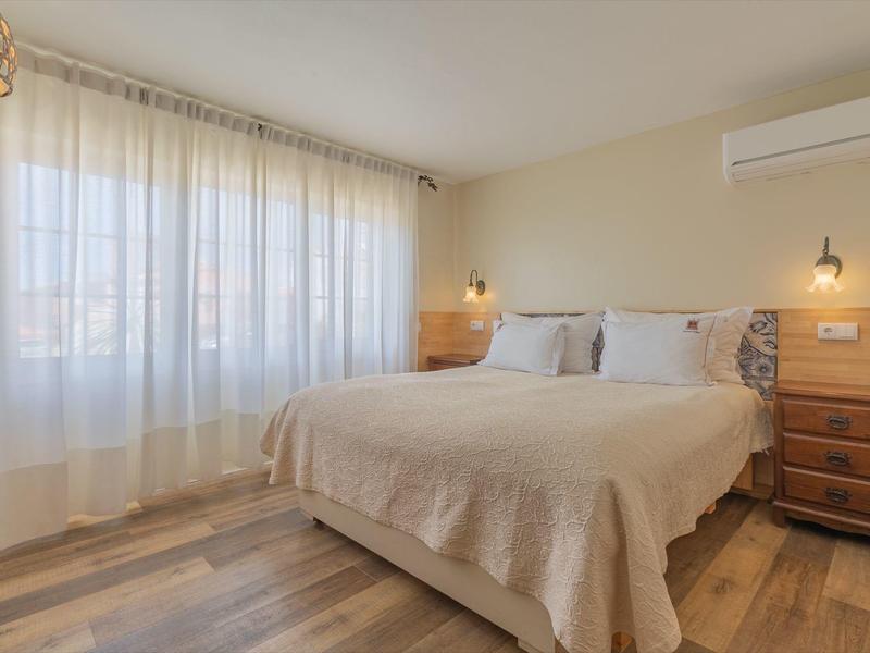 Helles Hotelzimmer mit Doppelbett, Holzboden und Gardinen an großen Fenstern.