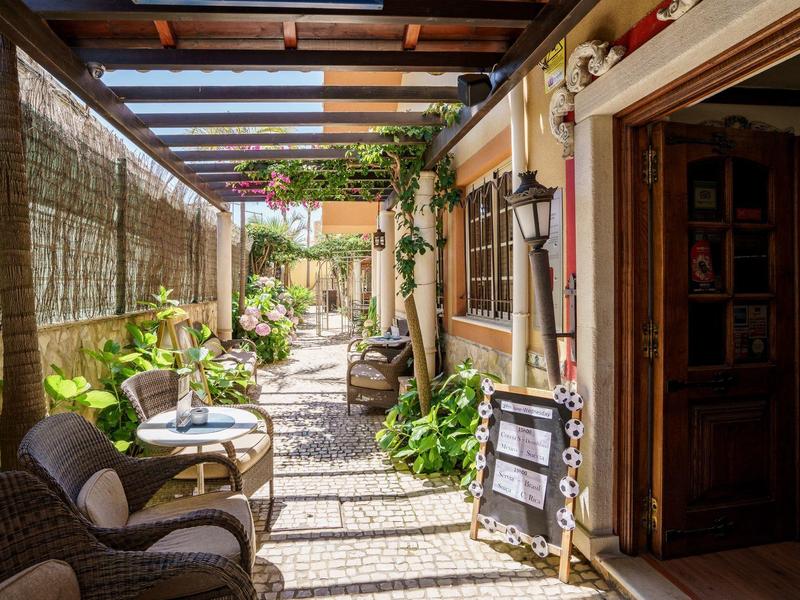 Gemütliche, schattige Terrasse mit Sitzgelegenheiten, Pflanzen und offenem Holztürrahmen.