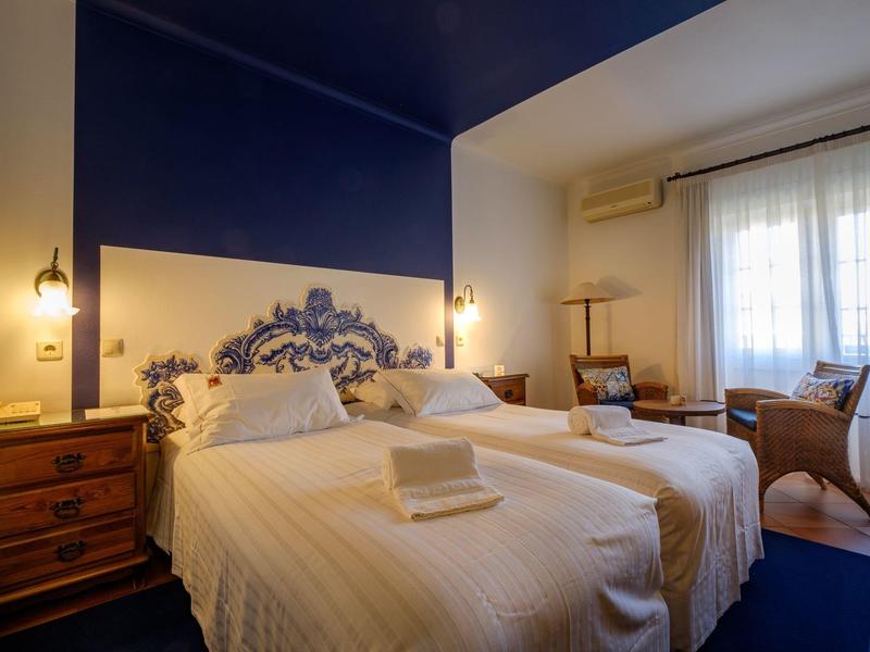 Zwei Einzelbetten mit weißen Bettdecken in einem Zimmer mit blauem Akzent an der Wand und Holzmöbeln.