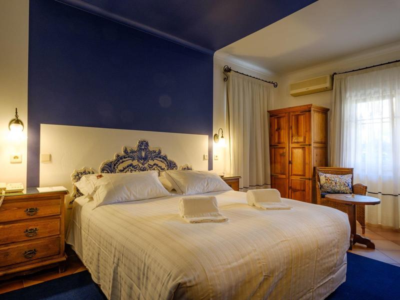 Helles Schlafzimmer mit blau-weißem Farbschema, großem Bett, Holzmöbeln und Vorhängen am Fenster.