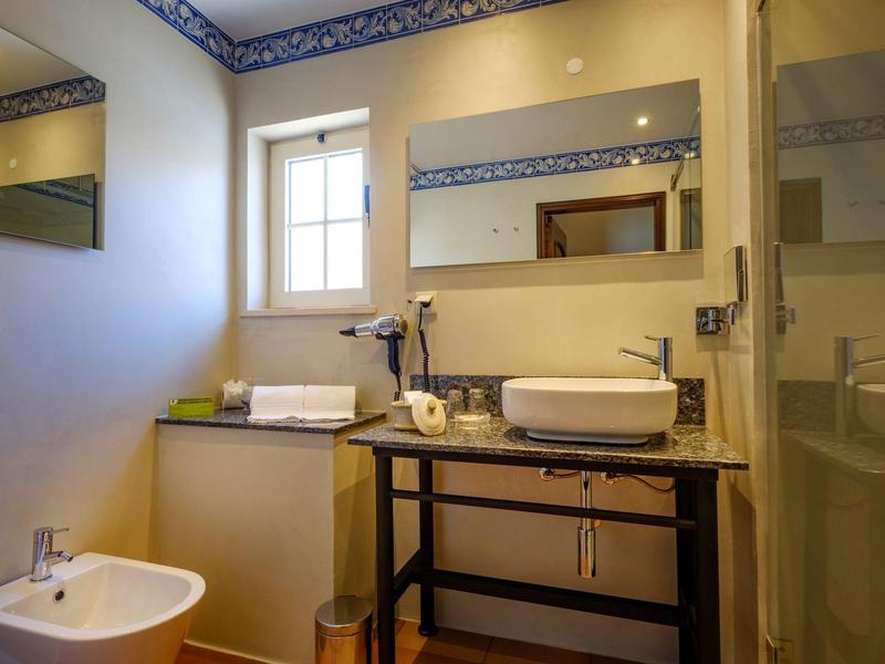 Helles Badezimmer mit weißem Bidet, Waschbecken auf Holzregal und Wasserkocher auf Theke.