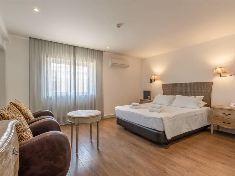 Modern eingerichtetes Hotelzimmer mit Doppelbett, zwei Sesseln und Holzboden, helle Wände und Tageslicht.